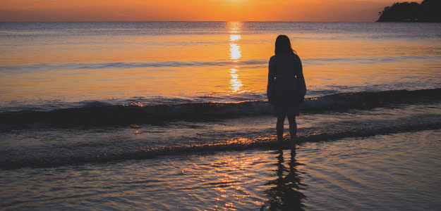 夕暮れの海に佇む人の写真